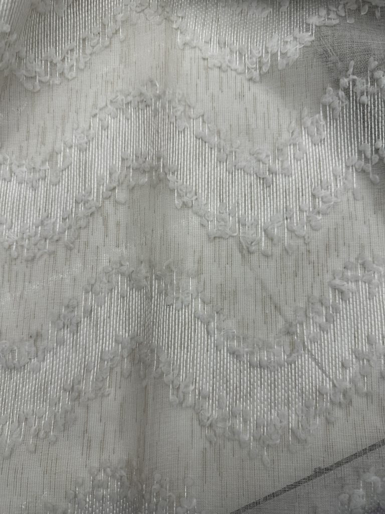 Elegant white curtain fabric with intricate embroidery and textured patterns.
