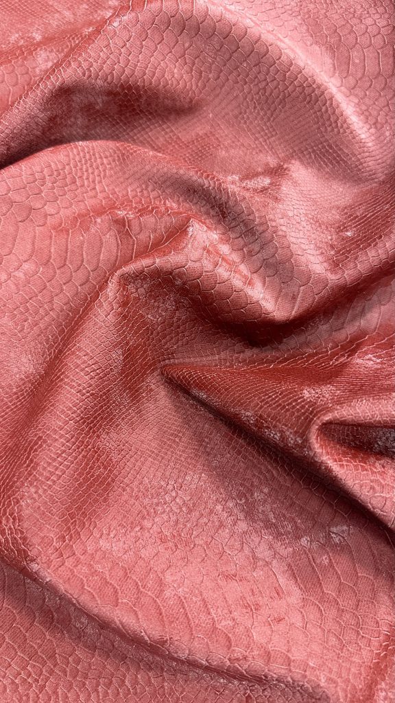 Close-up of snake print leather in pinkish hue with textured scales.